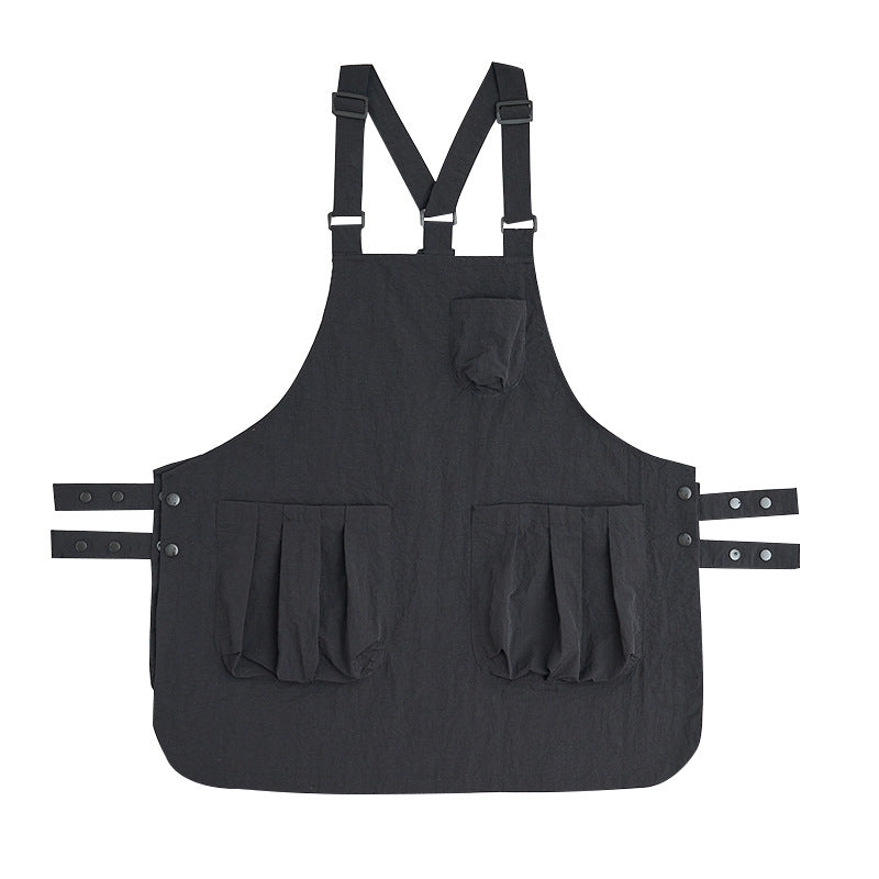 Black sleeveless kitchen apron laid flat with cross-back straps